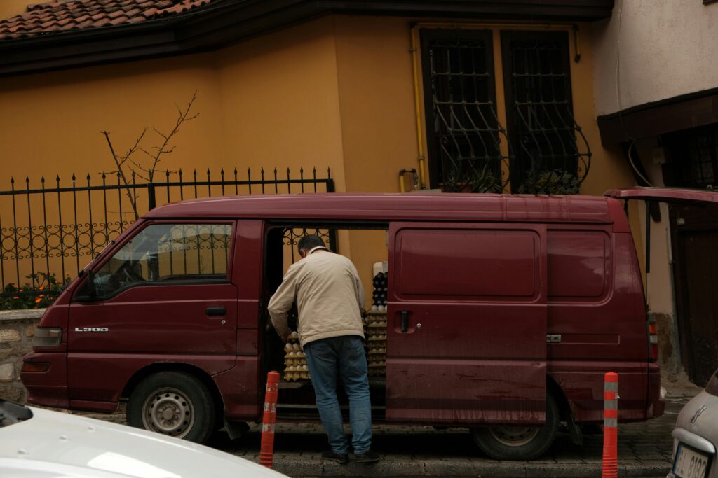 A man unloading cartons of eggs from a red vehicle parked on a street, incorporating daily commerce activities.