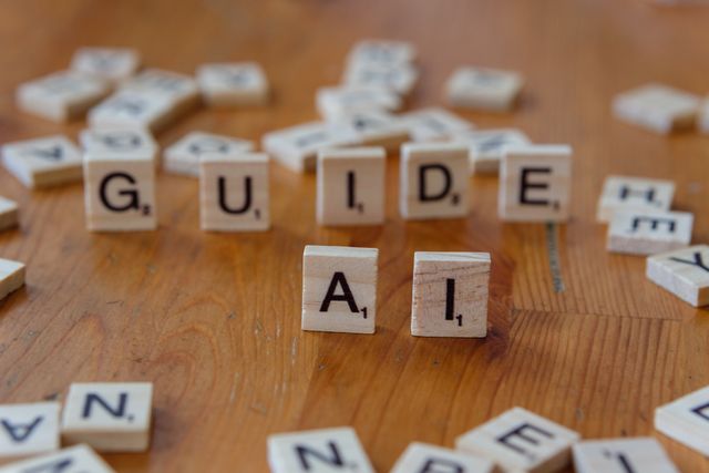Scrabble letters spelling 'GUIDE' and 'AI' on a wooden surface, suggesting direction and technology.