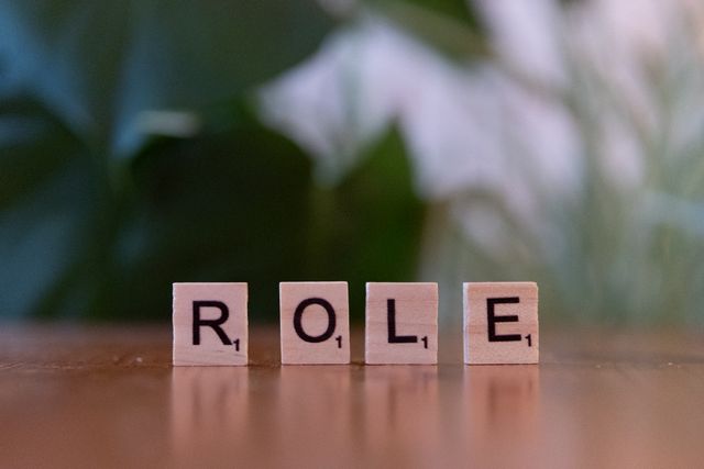 Close-up of Scrabble tiles spelling 'ROLE' on a wooden surface with a blurred background.